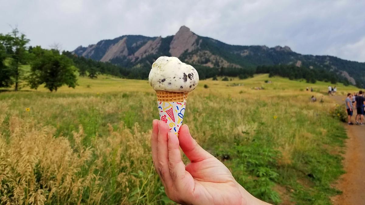 Hand holding an ice cream cone in front of the Flatirons