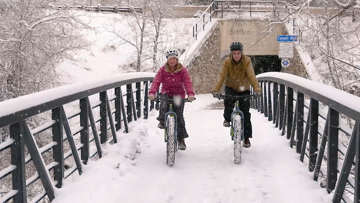 Two People Fat Biking Across A Snowy Bridge in Boulder