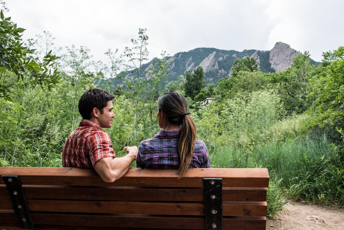 isitors take a moment to chat on a bench with the Flatirons rising up in the distance.