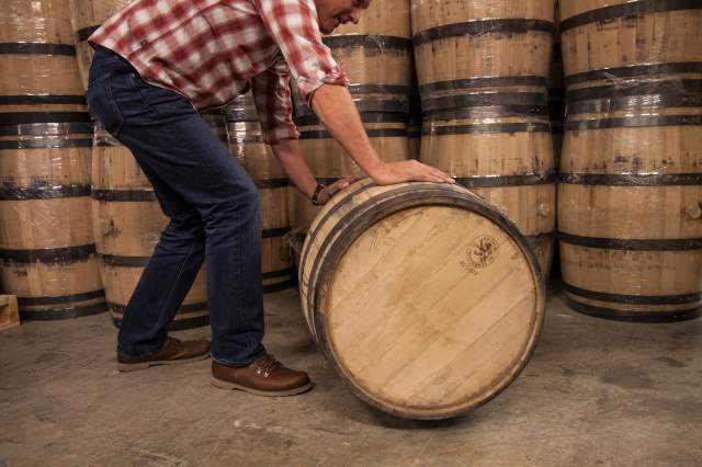 A man rolls a barrel of aging spirits at Vapor Distillery in Boulder, CO