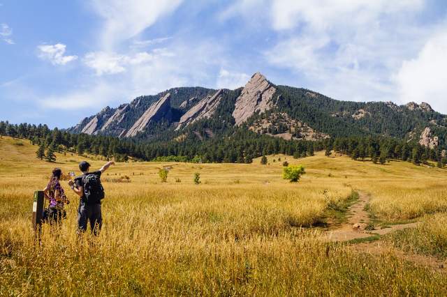 Two hikers pointing at the mountains at the base of the Flatirons