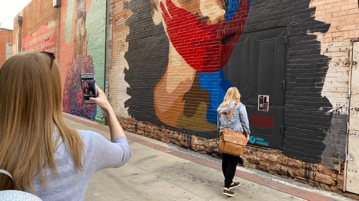 Woman taking a photo of a woman in front of Street Wise Murals Behind Boulder Theater